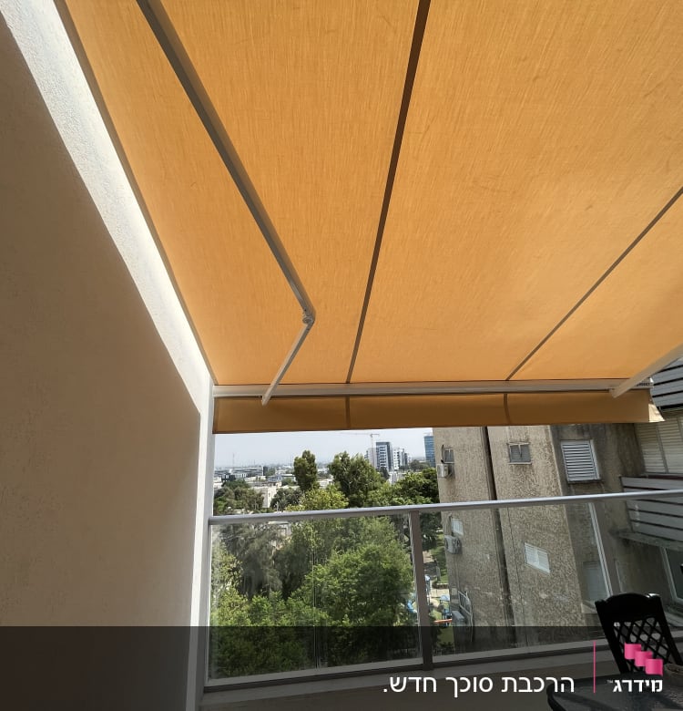 סוכך כתום תלוי מעל מרפסת עם מעקה זכוכית.